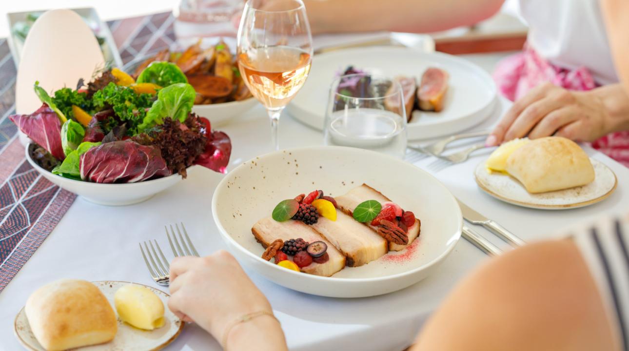 Two people enjoying their meals with a bowl of salad and glass of wine