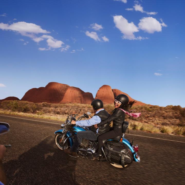 couple riding on the back of a Harley with Uluru in the background