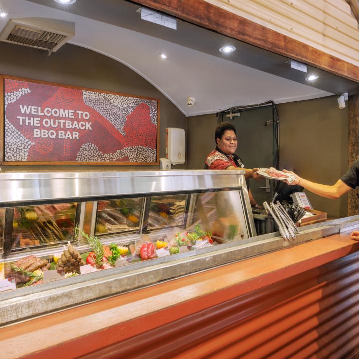 Two women getting handed a piece of meat by staff in front of the meat selection and chef