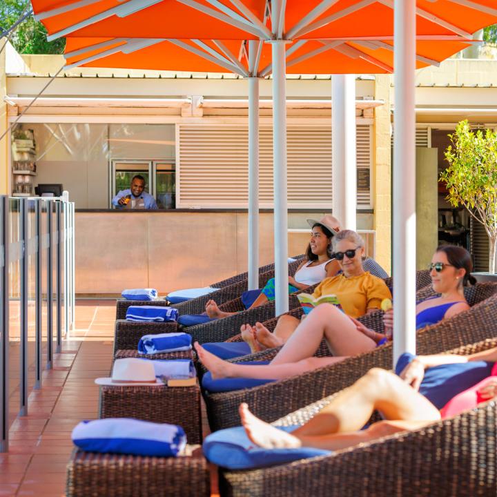Four females relaxing in egg chairs at Pira Pool Bar while a bar attendant pours a ginger beer into a glass