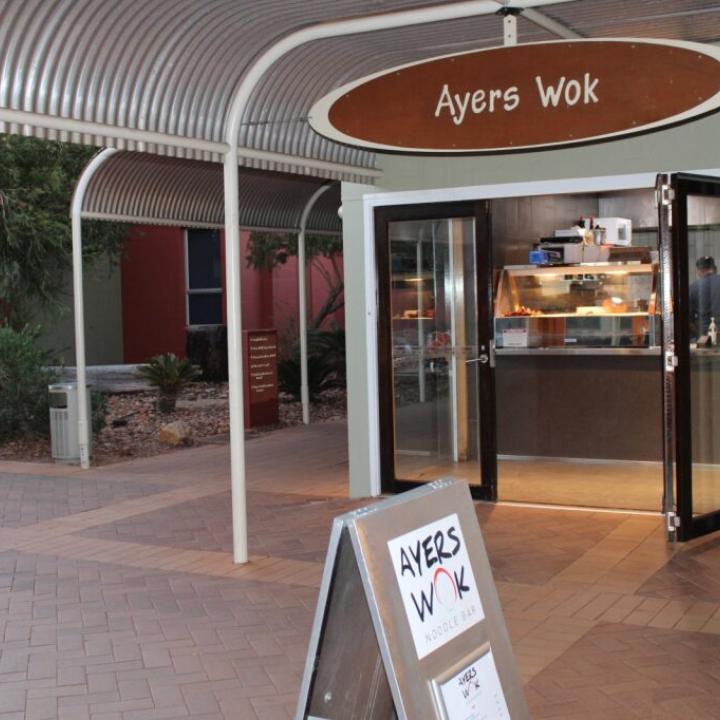 The front entrance of Ayers Wok with sliding doors open and a chef in the ktichen, with a sign outside,