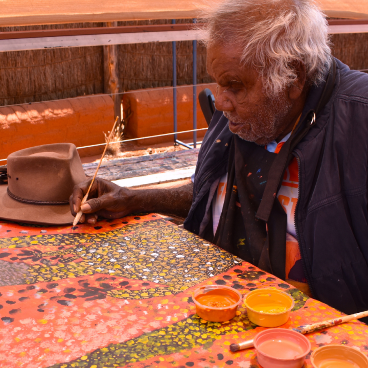 Reggie Uluru sitting down and painting on a large canvas