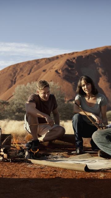 a group sitting outside by Ayers Rock