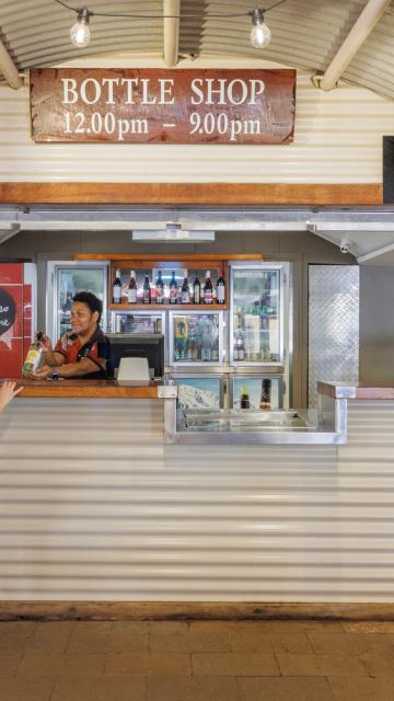 A women who works out the bottle shop is showing a customer a bottle of wine