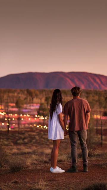 Couple standing in front of the Field of Light exhibition with Uluru in the background