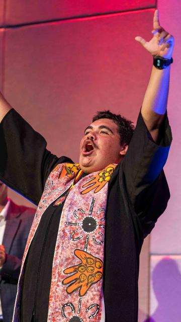 A NITA graduate with their hands up holding their certificate and people clapping in the background